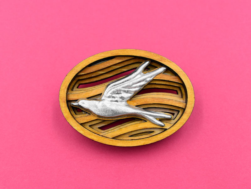 空を飛ぶツバメをモチーフとしたブローチの正面（赤い背景）。