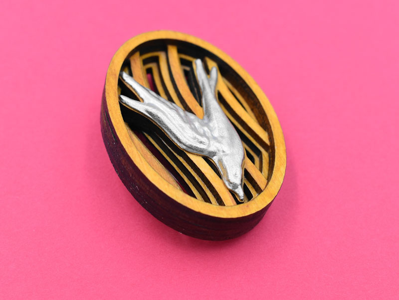 空を飛ぶツバメをモチーフとしたブローチの斜めからの画像1（赤い背景）。